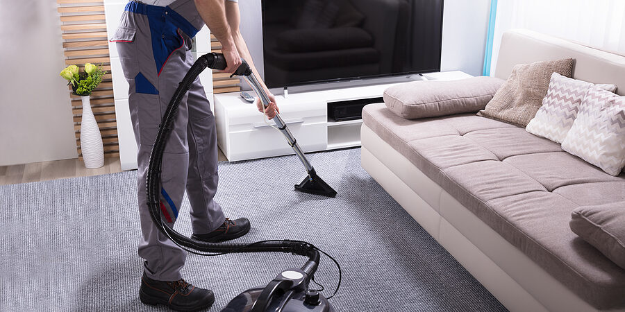 Close-up Of A Male Janitor Using Vacuum Cleaner For Cleaning The Carpet In Living Room